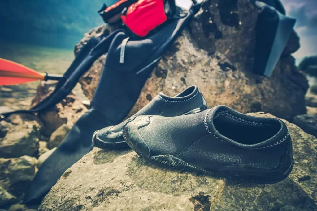Ce qu'il faut porter pour faire du kayak : une combinaison et des chaussures de kayak qui sèchent sur un rocher.