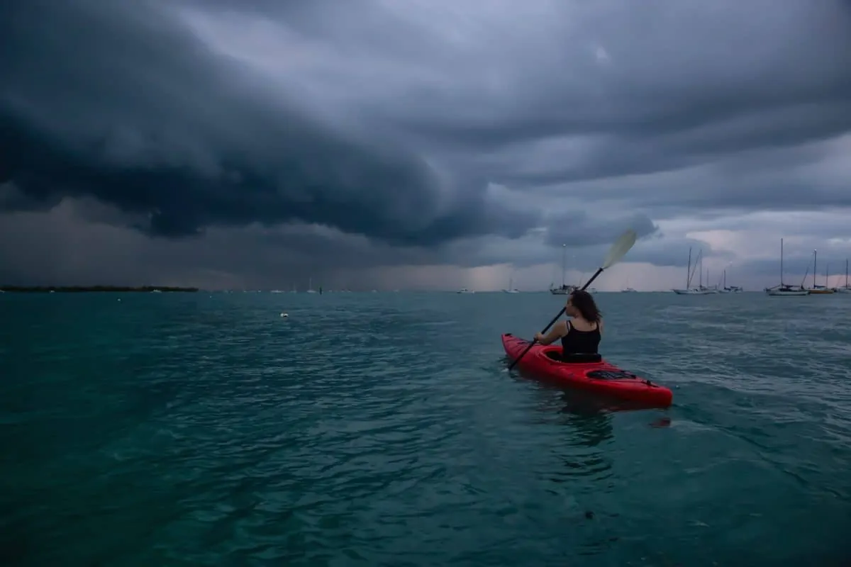 Une fille aventureuse sur un kayak rouge fait du kayak en direction d'un orage.